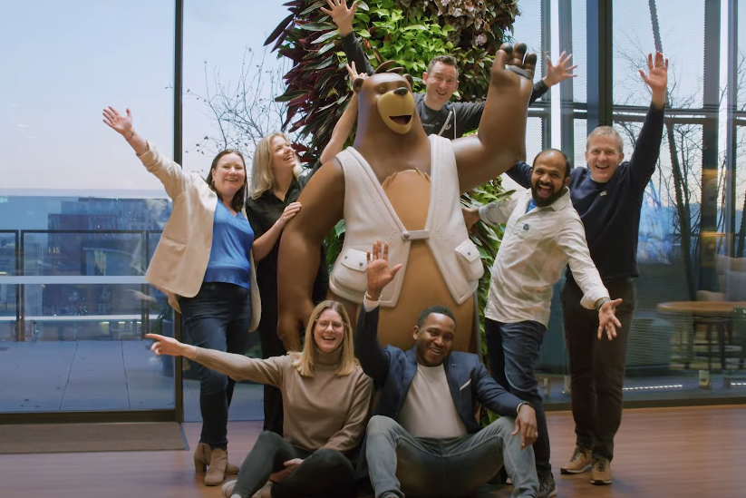 A group of people poses with raised arms around Salesforce mascot Cozy the bear